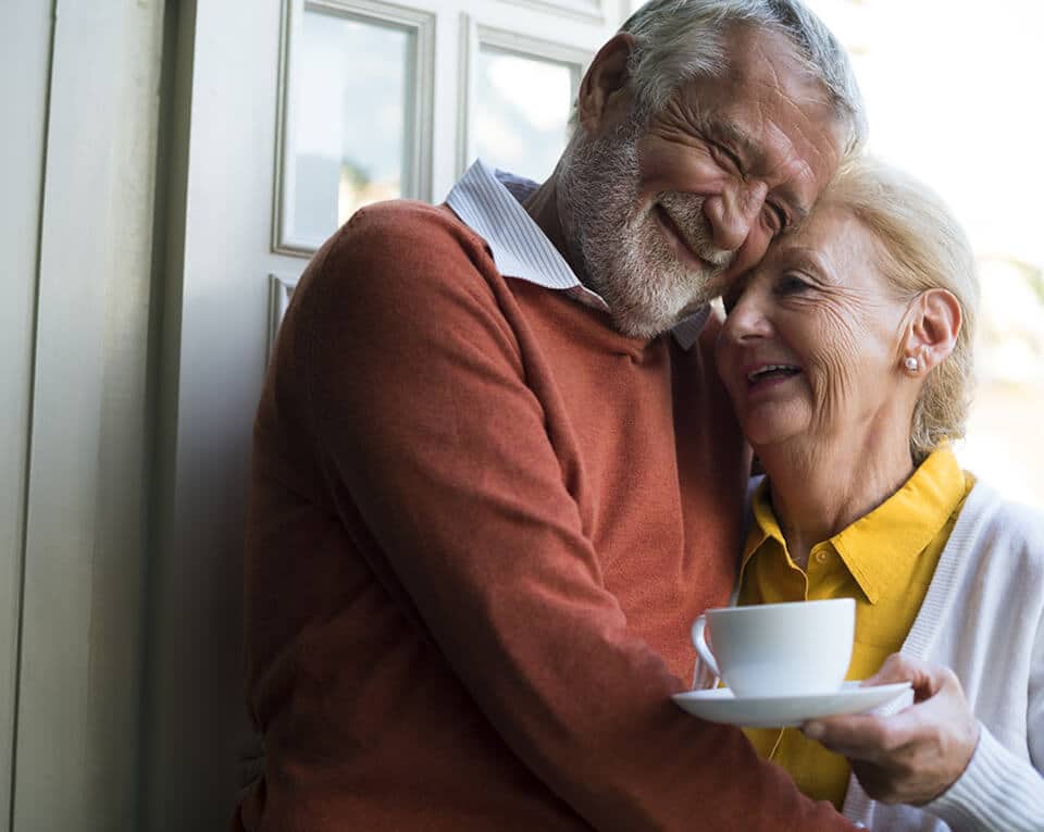 elderly couple hugging with a cup of coffee